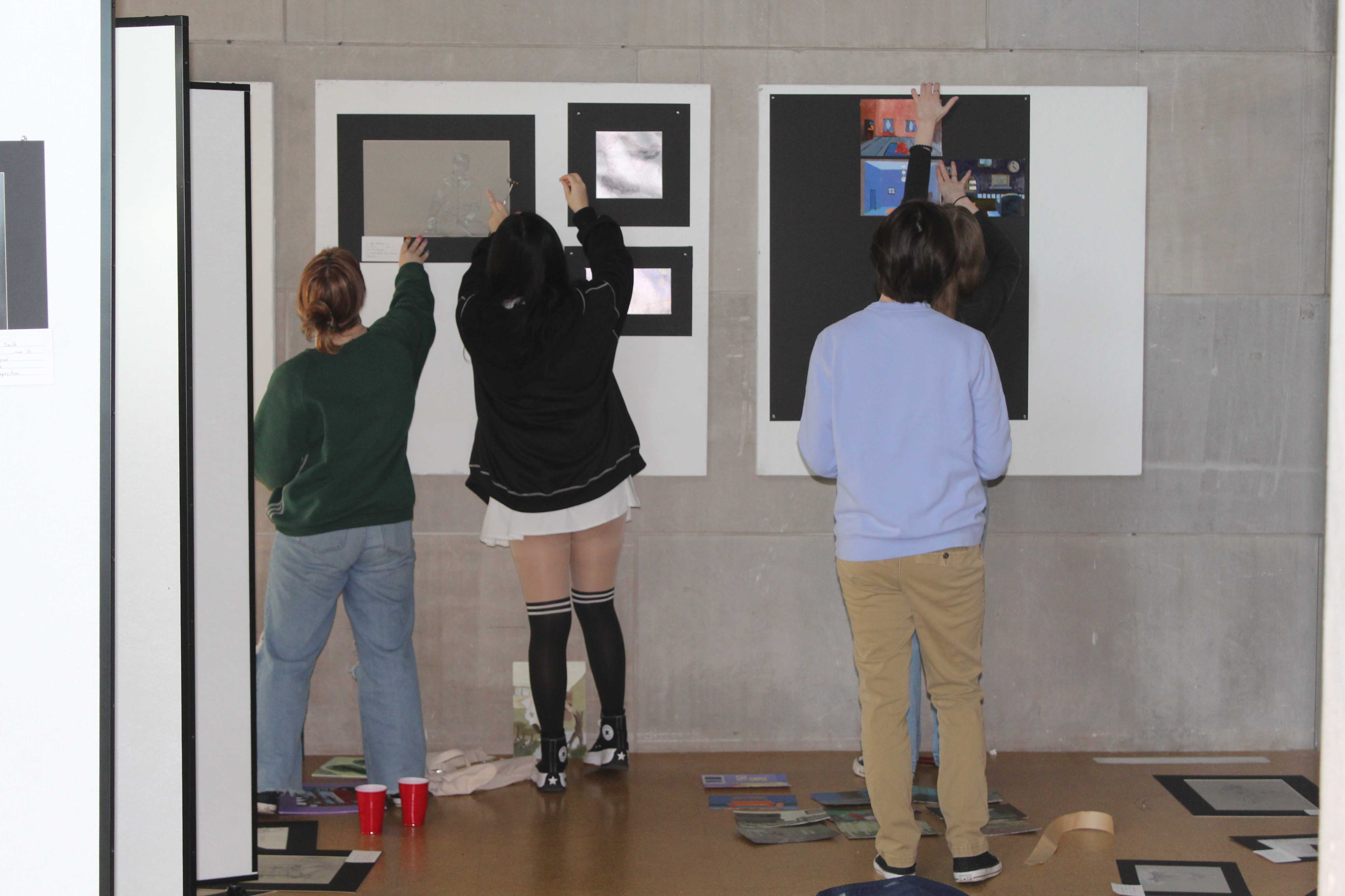 Students are putting up pieces of artwork at the gallery for the upcoming art show